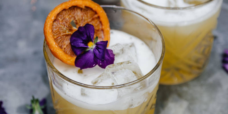 cocktail served with orange garnish and edible flower